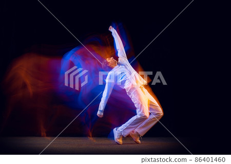 Sportive, emotional man, dancer dancing hip-hop isolated on dark background in mixed neon light. Youth culture, hip-hop, movement, style and fashion, action. Sportive, emotional man, dancer dancing hip-hop isolated on dark background in mixed neon light. Youth culture, hip-hop, movement, style and fashion, action. 86401460