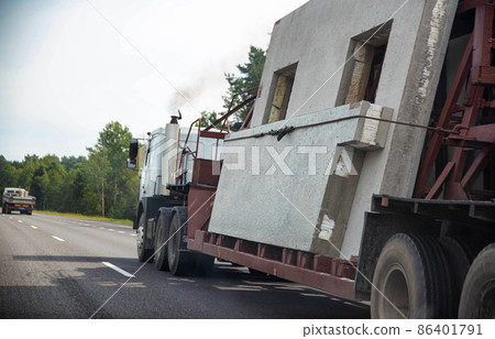 Transportation of reinforced concrete slabs for the construction of a panel house on the road against the background of a forest on a sunny summer day. Copy space for text Transportation of reinforced concrete slabs for the construction of a panel house on the road against the background of a forest on a sunny summer day. Copy space for text 86401791