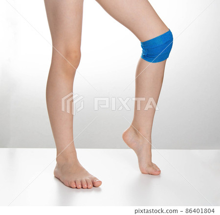 Blue elastic bandage on the knee joint on the child's leg. White background, treatment of knee pain and sprain, close-up 86401804