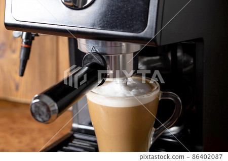 Making coffee with cappuccino milk in a cappuccino machine with a manual cappuccino maker on the background of a wooden table top. Close-up Making coffee with cappuccino milk in a cappuccino machine with a manual cappuccino maker on the background of a wooden table top. Close-up 86402087