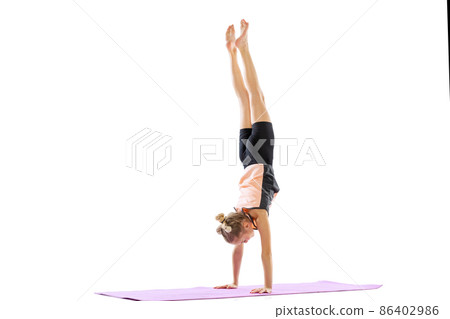 Portrait of sportive young girl, rhythmic gymnastics artist doing a handstand isolated on white studio background. Grace in motion, action. Portrait of sportive young girl, rhythmic gymnastics artist doing a handstand isolated on white studio background. Grace in motion, action. 86402986