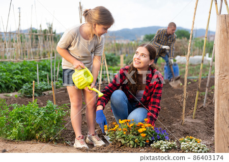 Mother and daughter watering plants at garden closeup Mother and daughter watering plants at garden closeup 86403174