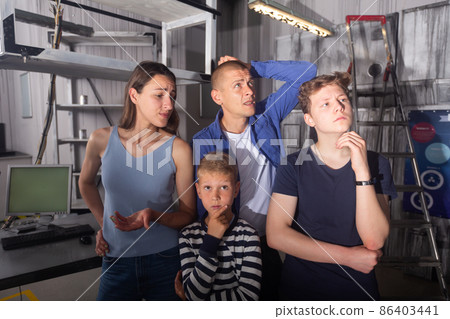 Close-knit family with children thinks, trying to find a solution to the puzzle in the quest room, to get out of there Close-knit family with children thinks, trying to find a solution to the puzzle in the quest room, to get out of there 86403441