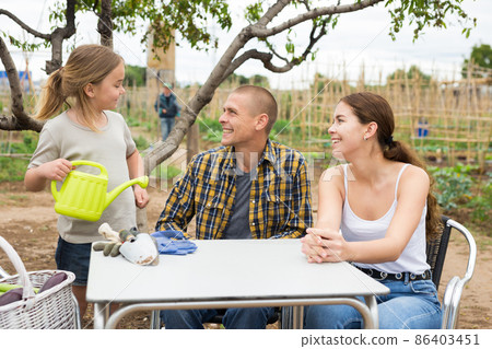 Friendly family sitting at the table after working in vegetable garden Friendly family sitting at the table after working in vegetable garden 86403451