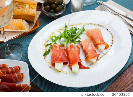 Spanish dish - rolls of iberian jamon stuffed with melon served with arugula 86403595