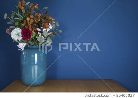 Blue vase on wooden table with plastic fake flower bouquet near blue wall, modern stylish decoration in living room with copy space. Home decoration concept 86405027