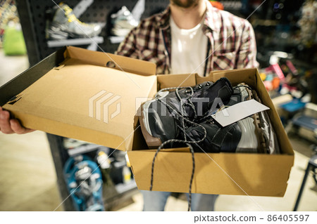 Store clerk helping customer try hiking boots at outdoors equipment shop. Salesman demonstrating trekking and hiking footwear for outdoor trails. Consultant help choose hiking boots in sports store Store clerk helping customer try hiking boots at outdoors equipment shop. Salesman demonstrating trekking and hiking footwear for outdoor trails. Consultant help choose hiking boots in sports store 86405597