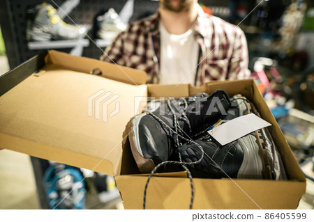 Caucasian male salesman consultant in outdoor store presenting hiking boots to buyer. A salesperson at a sports store helps a shopper to choose hiking boots. Seller in sporting goods store 86405599