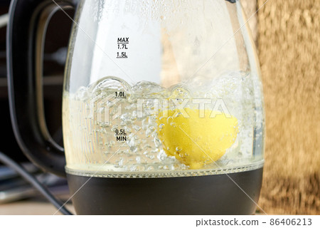 Half a yellow lemon is boiled in a glass electric kettle for descaling 86406213