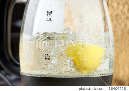 Half a yellow lemon is boiled in a glass electric kettle for descaling 86406218