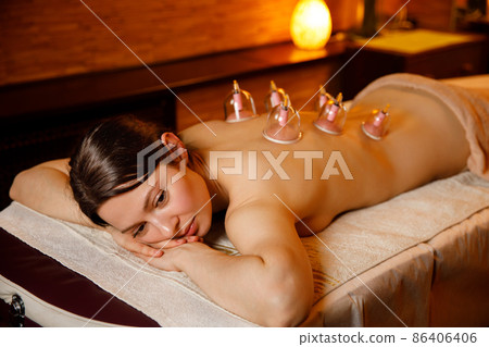 A young woman relaxes in a massage parlor. Vacuum cups of medical cupping therapy on woman back, close up, traditional chinese medicine. A young woman relaxes in a massage parlor. Vacuum cups of medical cupping therapy on woman back, close up, traditional chinese medicine. 86406406