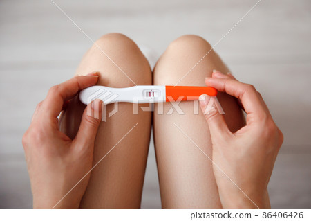 A sad young woman holds a pregnancy test in her hand. The concept of unwanted pregnancy. A sad young woman holds a pregnancy test in her hand. The concept of unwanted pregnancy. 86406426