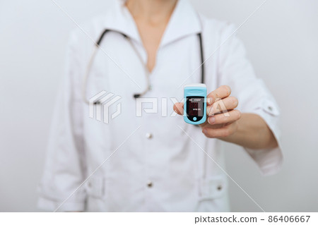 Pulse oximeter with hand of doctor isolated on white. The concept of portable digital device to measure person's oxygen saturation. Measuring oxygen saturation, pulse rate and oxygen levels 86406667