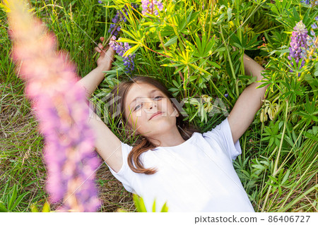 Happy teenage girl smiling outdoor. Beautiful young teen woman resting lying on summer field with blooming wild flowers green background. Free happy kid relaxing and enjoying nature 86406727