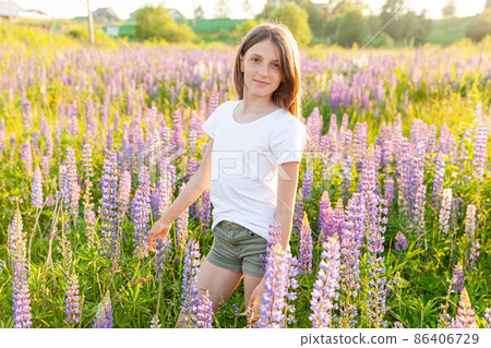 Happy teenage girl smiling outdoor. Beautiful young teen woman resting on summer field with blooming wild flowers green background. Free happy kid teenager girl, childhood concept 86406729