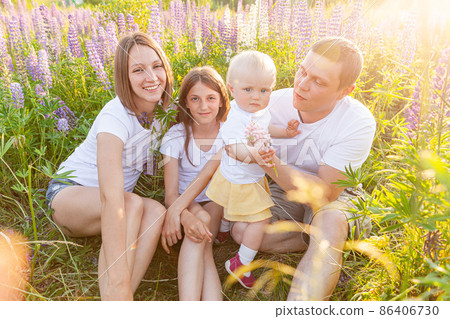 Happy family mother father embracing kids outdoor. Woman man baby child and teenage girl sitting on summer field with blooming flowers background. Happy family mom dad and daughters playing on meadow Happy family mother father embracing kids outdoor. Woman man baby child and teenage girl sitting on summer field with blooming flowers background. Happy family mom dad and daughters playing on meadow 86406730
