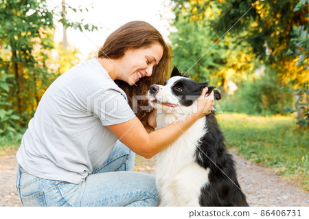 Smiling young attractive woman playing with cute puppy dog border collie on summer outdoor background. Girl holding embracing hugging dog friend. Pet care and animals concept 86406731