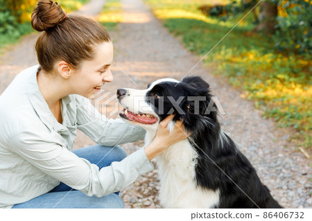 Smiling young attractive woman playing with cute puppy dog border collie on summer outdoor background. Girl holding embracing hugging dog friend. Pet care and animals concept Smiling young attractive woman playing with cute puppy dog border collie on summer outdoor background. Girl holding embracing hugging dog friend. Pet care and animals concept 86406732
