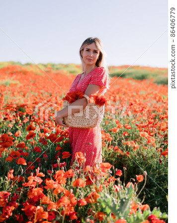 Caucasian blonde woman in a poppy field. Woman in red dress and handbag with wild flowers Caucasian blonde woman in a poppy field. Woman in red dress and handbag with wild flowers 86406779