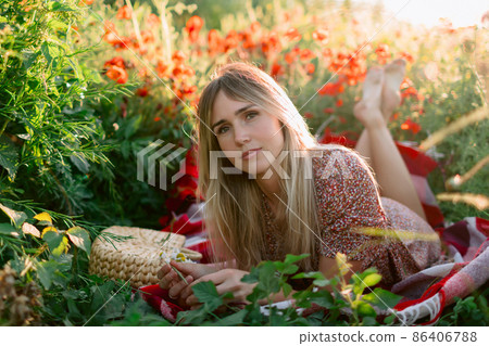 Portrait woman in outdoor on plaid with poppy flowers at sunset. Woman in dress with field flowers 86406788