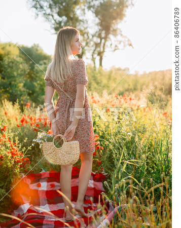 Blonde woman in outdoor on plaid with poppy flowers at sunset. Woman with field flowers 86406789