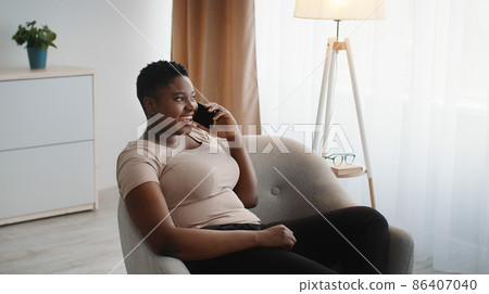Great mobile connection. Young carefree chubby african american woman enjoying pleasure talk with friends via cellphone 86407040