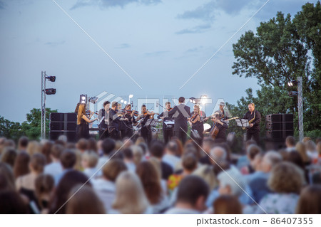 Orchestra performing live concert for audience under blue sky 86407355