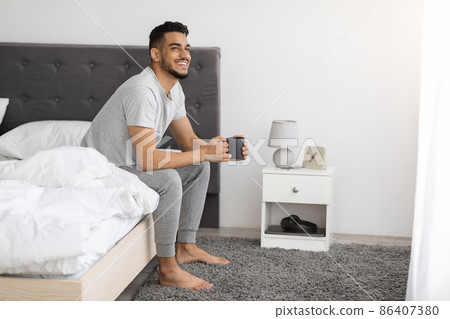 Happy Morning. Smiling Arab Man Sitting In Bed With Cup Of Coffee Happy Morning. Smiling Arab Man Sitting In Bed With Cup Of Coffee 86407380