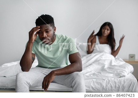 Sad millennial african american woman sits on bed swear her offended husband in bedroom interior Sad millennial african american woman sits on bed swear her offended husband in bedroom interior 86407423
