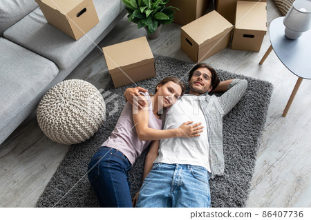 Tired smiling european millennial husband and wife rejoice buying new own apartment, lie on floor Tired smiling european millennial husband and wife rejoice buying new own apartment, lie on floor 86407736