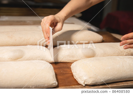 Close-up of a baker's female hands cutting a loaf of dough into a loaf of bread with a blade before baking in the oven. Craft craft bread production 86408580