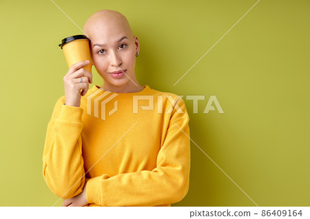 thoughtful young hairless female holding cup of coffee in hands looking at camera 86409164