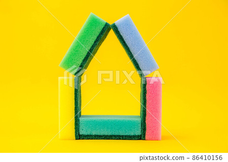 Multicolored sponges for cleaning folded in the shape of a house on a yellow background. Space for text 86410156