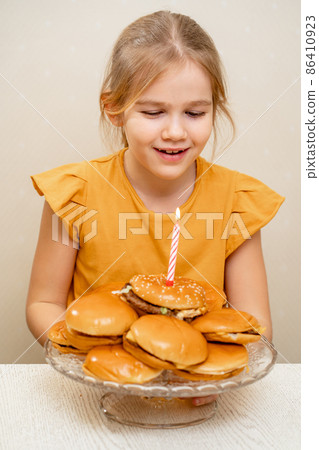 a funny little girl makes a wish and blows out a candle on a hamburger cake. a funny little girl makes a wish and blows out a candle on a hamburger cake. 86410923