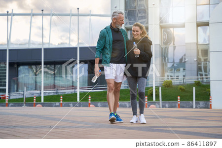 Full length shot of active middle aged couple in sportswear looking cheerful while walking together outdoors after gym workout 86411897