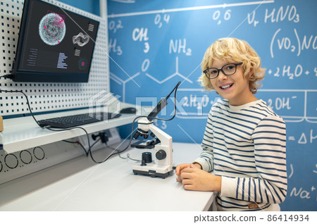 Boy in glasses looking at camera standing near microscope 86414934