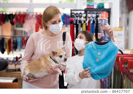 Woman in mask in pet store during shopping with her daughter with dog Woman in mask in pet store during shopping with her daughter with dog 86417707