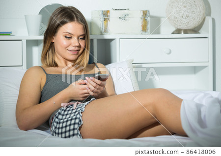 Smiling girl lying and using smartphone on bed in bedroom 86418006