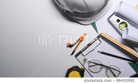 Top view glasses, blueprints, tape measure and hard hat on white table. 86420992