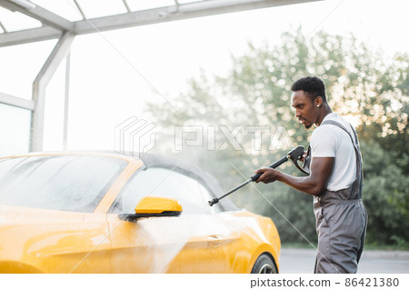 Washing outside rearview car mirror with high pressure water at self car wash service outdoors. Washing outside rearview car mirror with high pressure water at self car wash service outdoors. 86421380