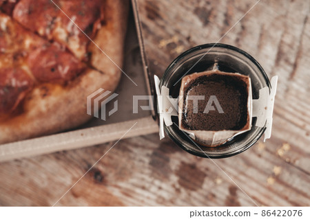 brewing coffee in a drip bag in a transparent glass, on a wooden background. Hot ground drip coffee, top view. Ground Ethiopian coffee in a reusable drip bag. brewing coffee in a drip bag in a transparent glass, on a wooden background. Hot ground drip coffee, top view. Ground Ethiopian coffee in a reusable drip bag. 86422076