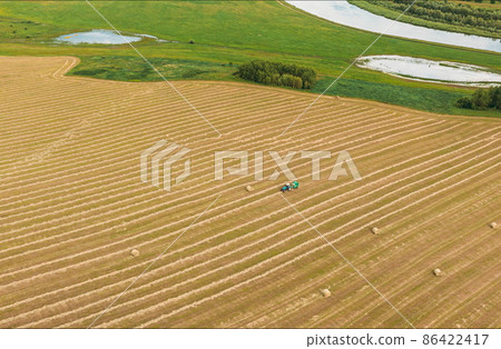4K Aerial View Tractor Collects Dry Grass In Straw Bales In Wheat Field. Special Agricultural Equipment. Hay Bales, Hay Making. 4K Aerial View Tractor Collects Dry Grass In Straw Bales In Wheat Field. Special Agricultural Equipment. Hay Bales, Hay Making. 86422417