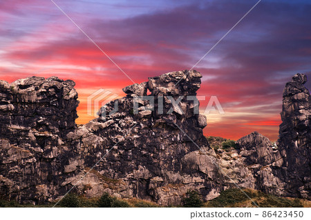 Surrealistic composition of the Devil's Wall near Thale in Saxony-Anhalt, Germany in front of a red and purple evening sky, rib of limestone on the edge of the Harz Mountains Surrealistic composition of the Devil's Wall near Thale in Saxony-Anhalt, Germany in front of a red and purple evening sky, rib of limestone on the edge of the Harz Mountains 86423450