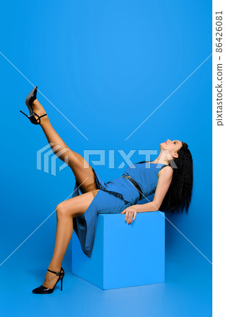Young woman in blue dress sitting on a cube and threw her leg in stocking up Young woman in blue dress sitting on a cube and threw her leg in stocking up 86426081