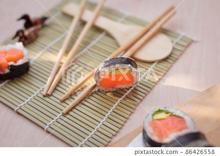 Closeup of sushi with chopsticks on a wooden background Closeup of sushi with chopsticks on a wooden background 86426558