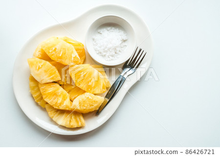 Closeup of a sliced pieces of fresh pineapple served with salt with isolated white table. Adding salt to pineapple suppresses the bitter flavor of the fruit. 86426721