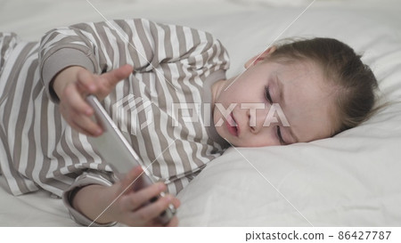 Child uses smartphone touch screen for education in bed Child uses smartphone touch screen for education in bed 86427787