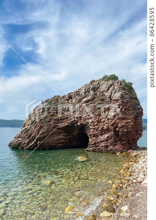 Landscape with lonely rock formation in the sea or ocean. Beautiful rock near coastline against blue sky, vertical image Landscape with lonely rock formation in the sea or ocean. Beautiful rock near coastline against blue sky, vertical image 86428595