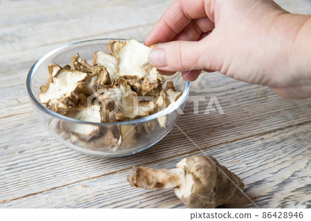 A woman 's hand over a plate with slices of dried jerusalem artichoke on a light wooden background . A woman 's hand over a plate with slices of dried jerusalem artichoke on a light wooden background . 86428946