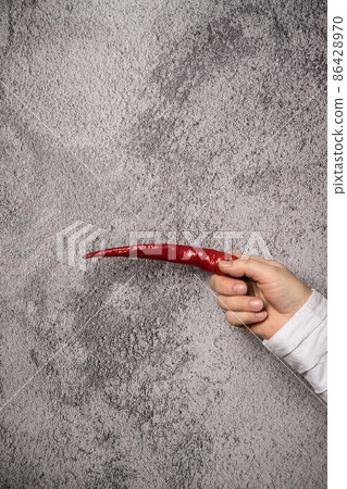 Pointing gesture of a woman's hand with hot pepper.Vertical arrangement 86428970